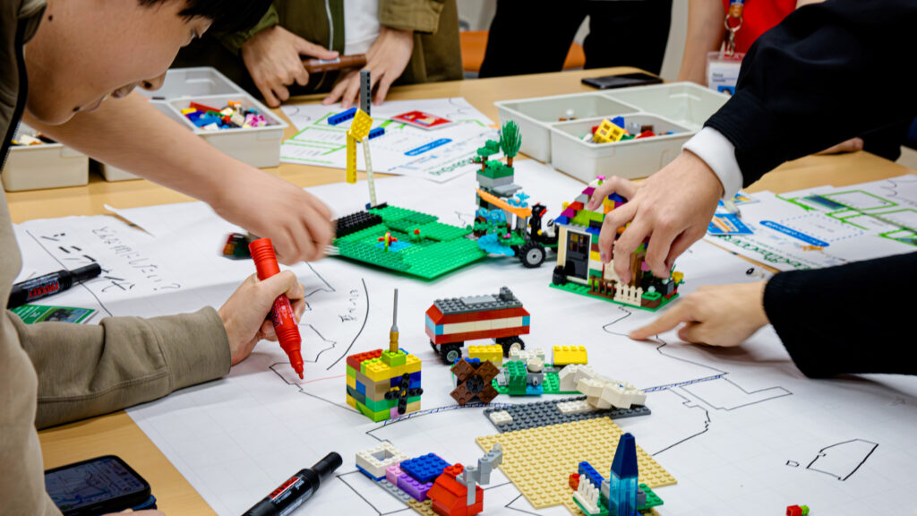 サステナブルなまちづくりワークショップ「サスネタ！」で、参加者がワークシート上にLEGOの建物や設備を配置し、街のプロトタイプを制作している様子