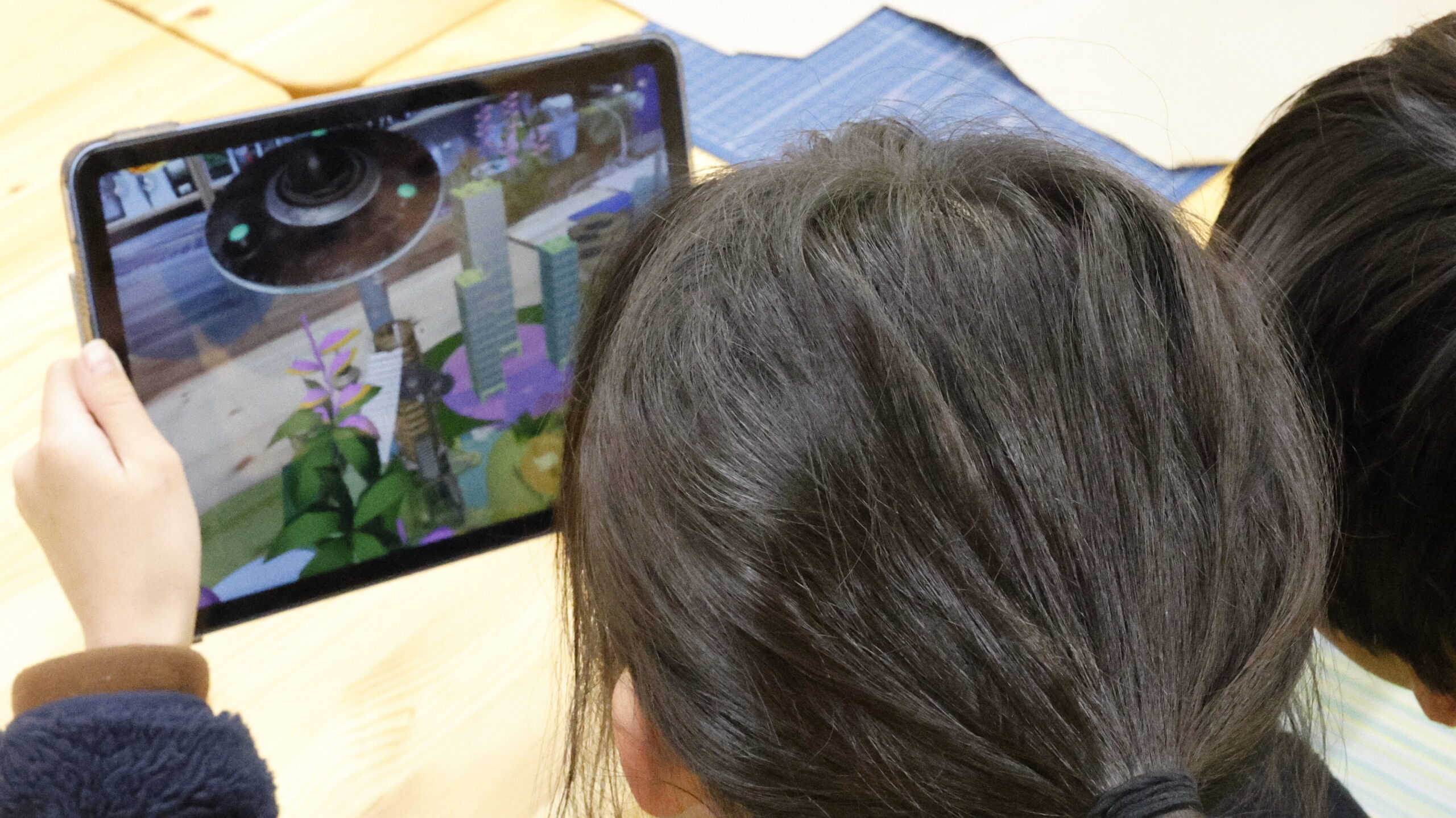 サステナブルなまちづくり教材「サスネタ！」で作った都市の3Dモデルを、タブレットのARで投影して配置やデザインを検討している場面