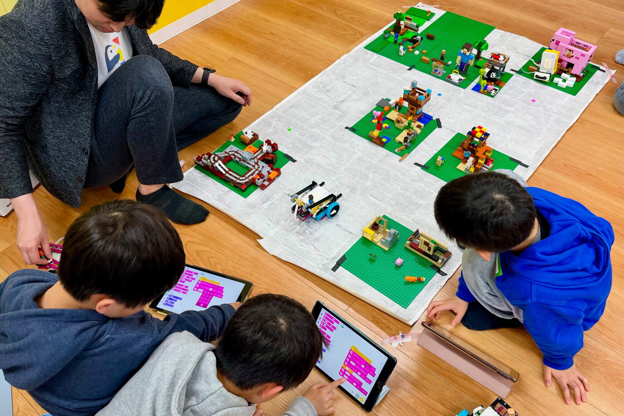 小学生たちがLEGOブロックで構成したマインクラフトの街を走る車のプログラムをタブレットで組むSTEAM教育。