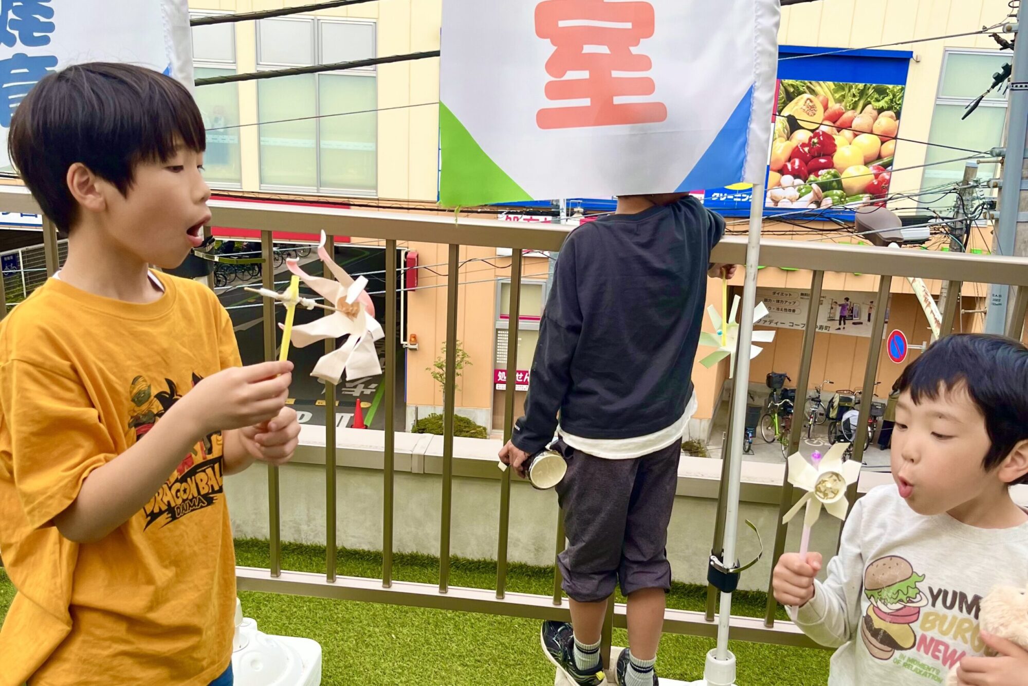 小学生が手作りの風車に息を吹きかけて風の力を観察するSTEAM工作と科学実験の様子。屋外で行われた探究活動の一場面。