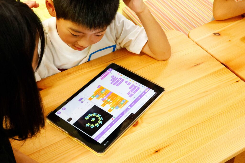 小学生がタブレットを使ってビジュアルプログラミングに取り組む様子。STEAM教育の現場でのデジタル学習体験。