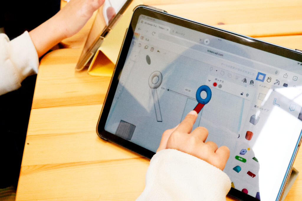 タブレット上のTinkercadでオリジナル文房具の3Dモデリングに挑戦する小学生の手元。STEAM教育の実践として、図工と技術を融合させたデジタル工作の様子。