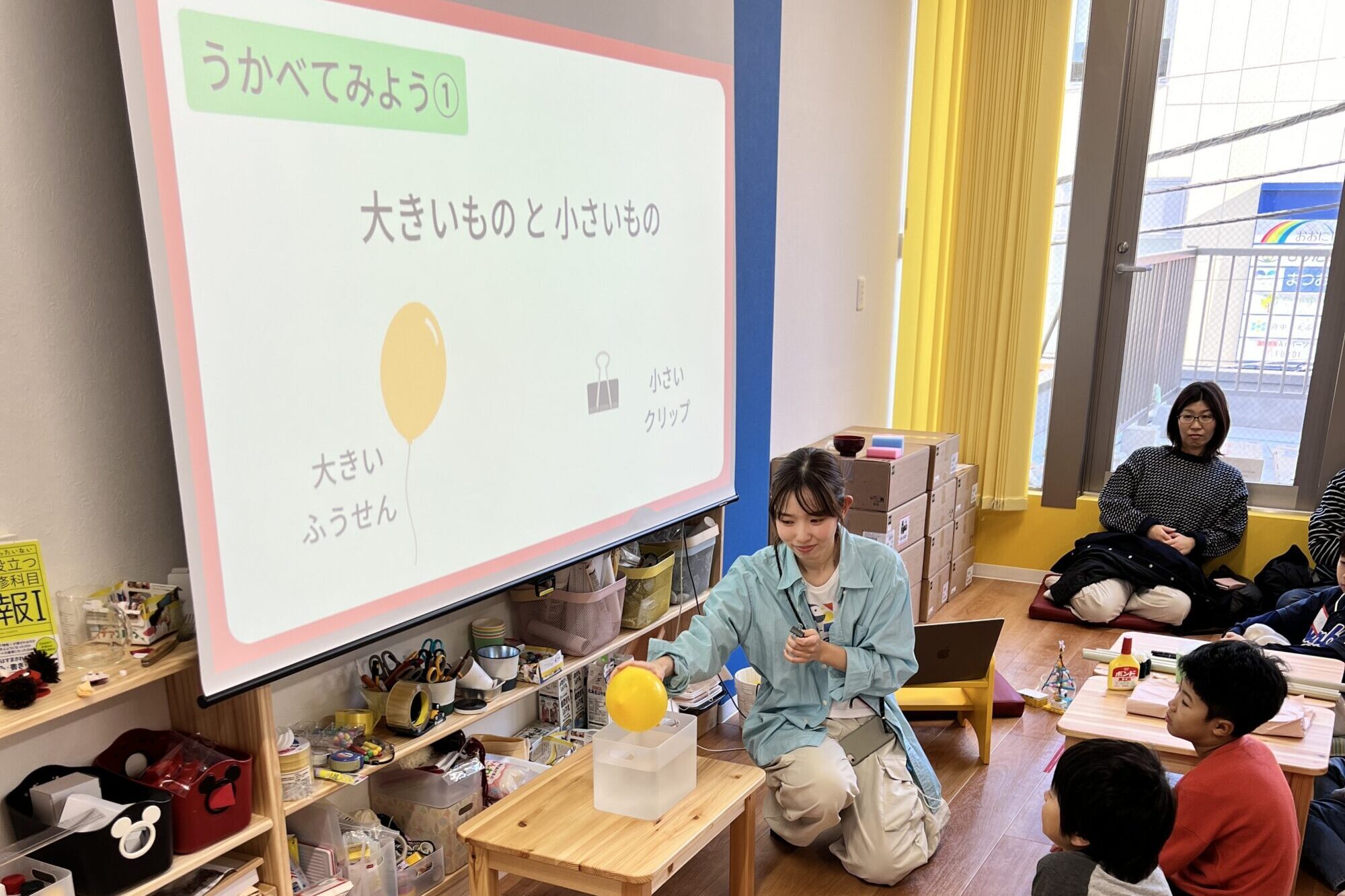 講師が風船とクリップを使って浮力の違いを実演する科学実験の授業風景。STEAM教育のサイエンス活動に集中する子どもたち。