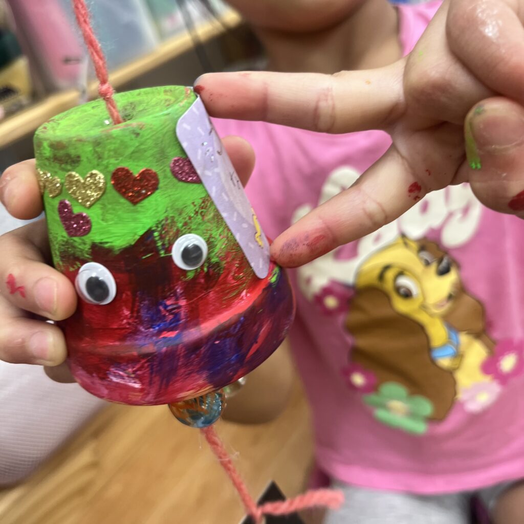 カラフルにデコレーションされた植木鉢風鈴を持つ子ども。シールや目玉パーツで楽しく仕上げた夏の工作