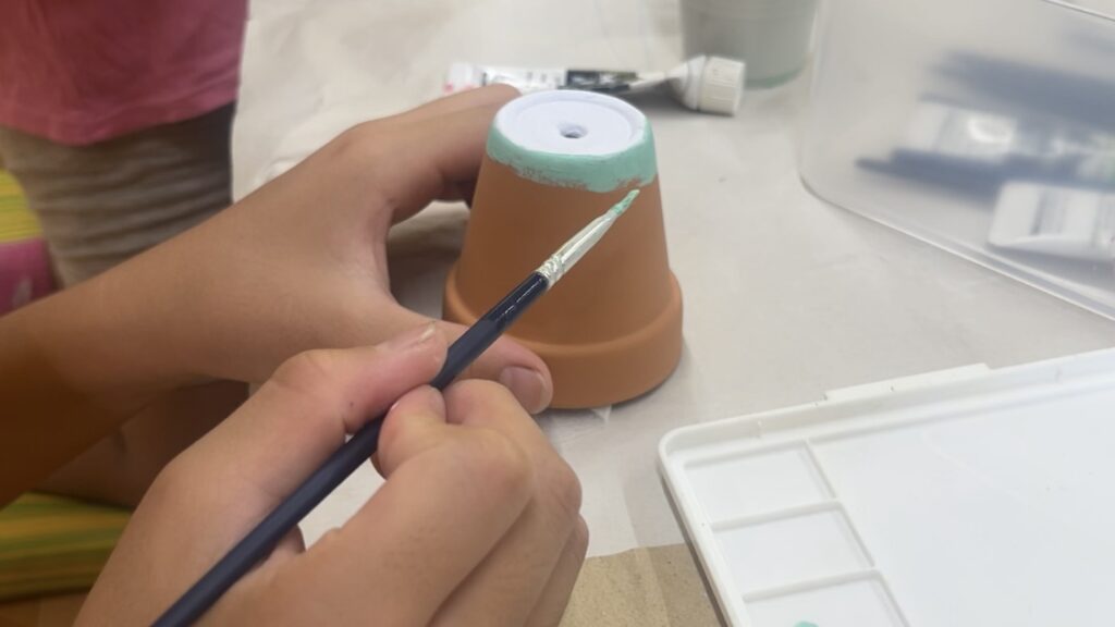 植木鉢に絵の具で色を塗る子どもの手元。親子で楽しむ風鈴づくりのデコレーション工程