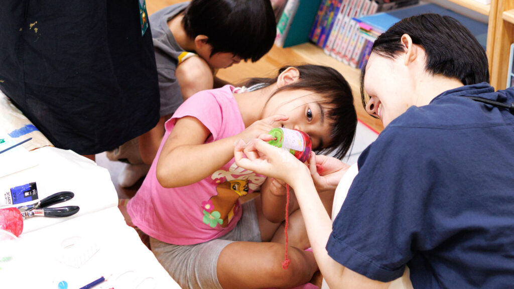 植木鉢風鈴を親子で制作する様子。お母さんと子どもが一緒にひもを結ぶ夏休み工作体験