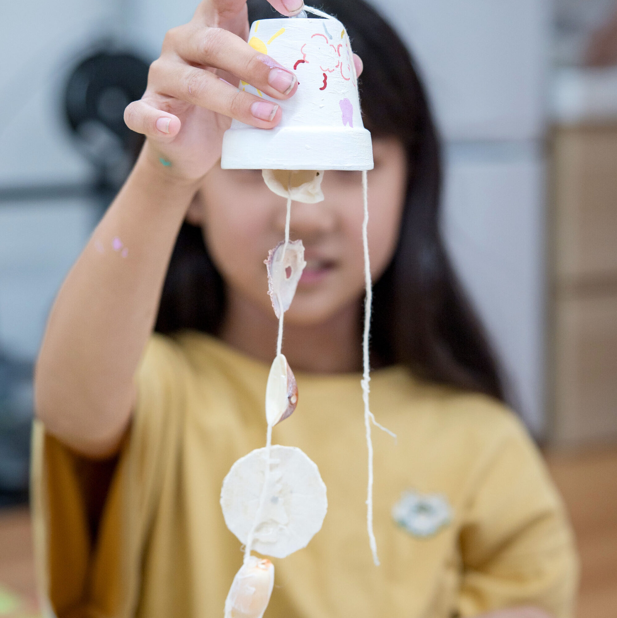 植木鉢風鈴を手に持つ子ども。貝がらを使った音が鳴る部分が見える夏休み工作の完成品