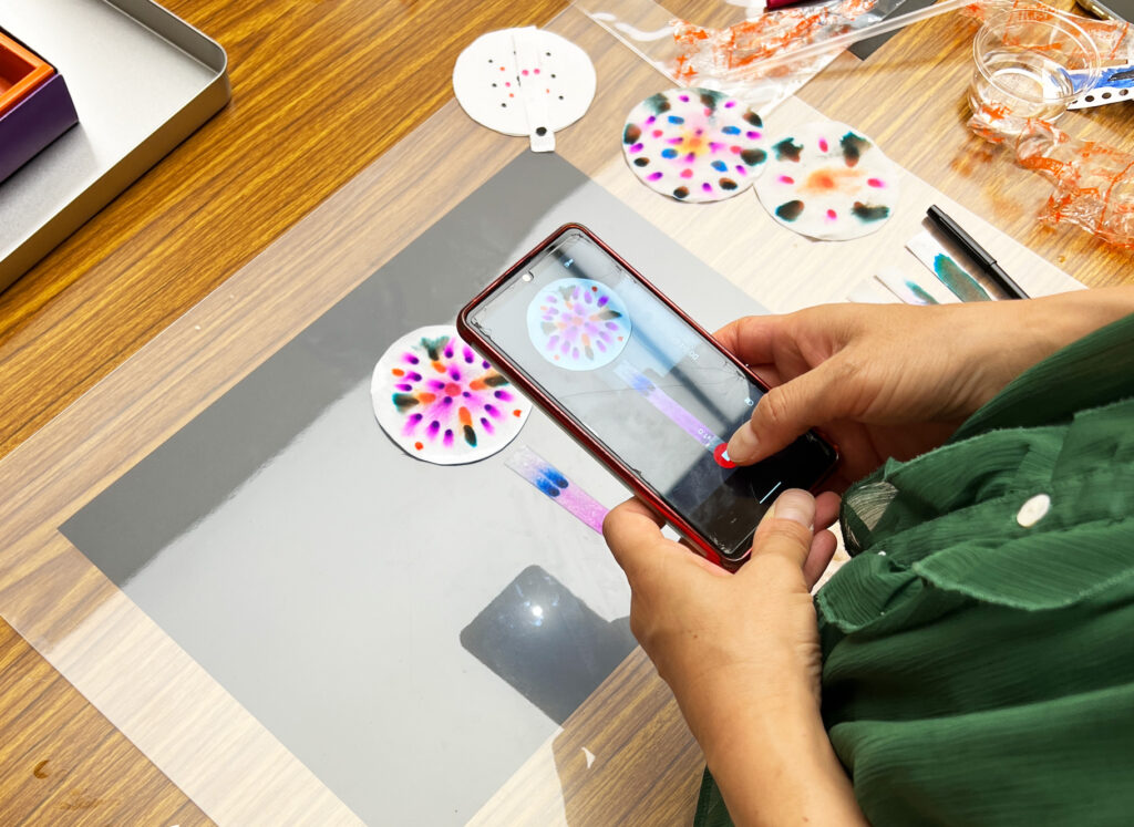 スマホで自由研究のペーパークロマトグラフィー実験を撮影する様子。色が広がる紙の花火を記録。