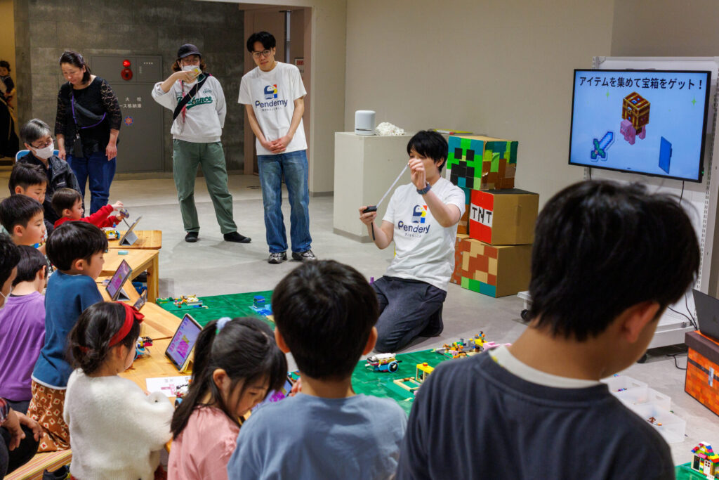 プログラミングイベントで参加者の小学生に優しく教える男性講師の様子