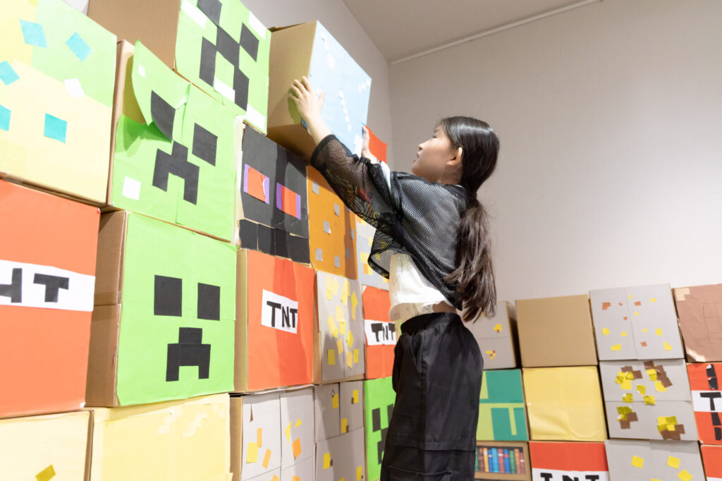 自分で工作したマイクラ風の元素ブロックを特設空間に笑顔で設置する小学生の女の子